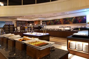 Un espace buffet doté de plusieurs points de service, un grand tableau abstrait accroché au mur et une variété de plats présentés dans des bols.