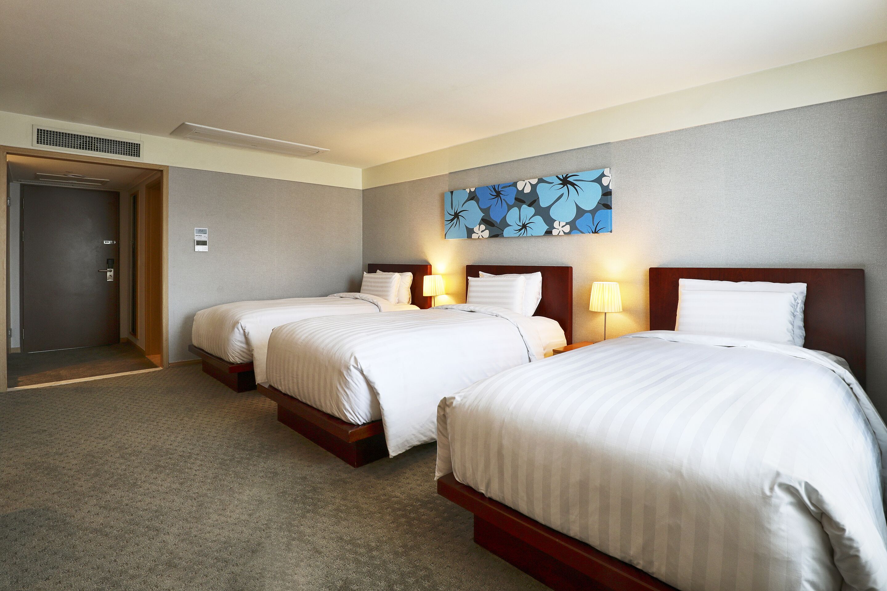 A hotel room with two beds, a door, and a wall-mounted artwork.