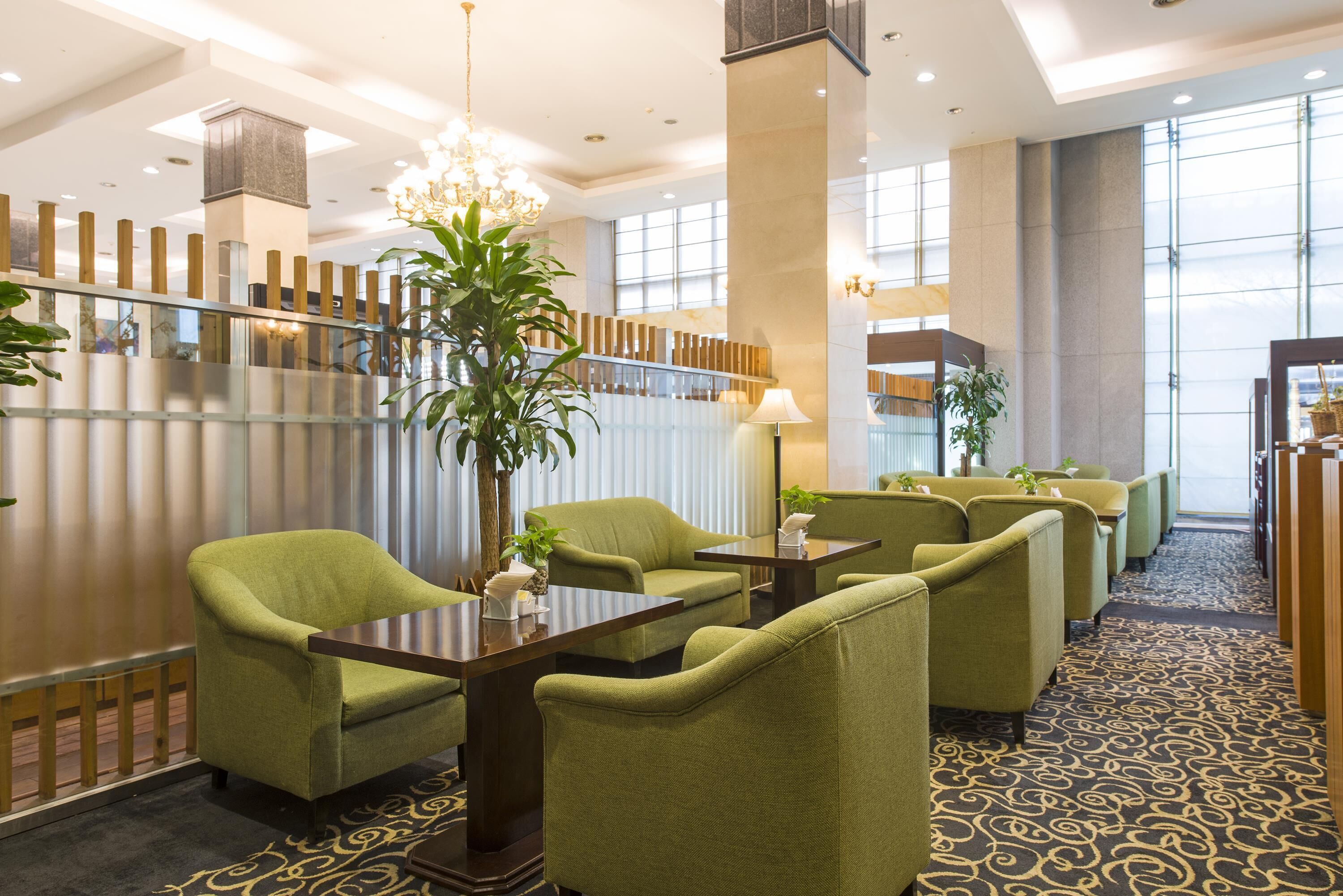 Eine Hotelhalle mit grünen, gepolsterten Sesseln, einem hölzernen Empfangstresen und einer großen Pflanze im Topf.