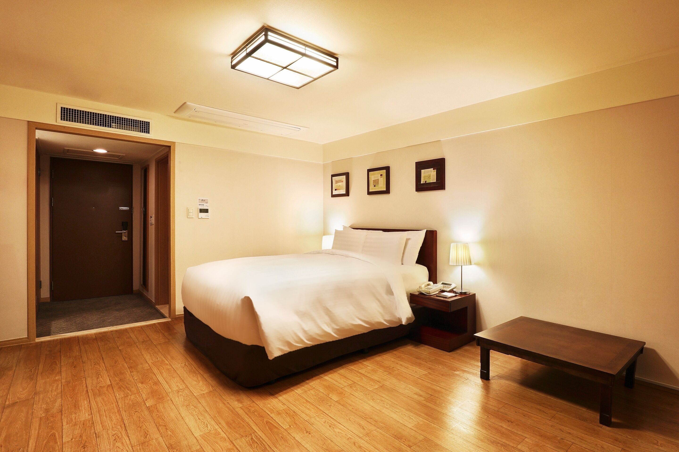 A hotel room with a bed, bedside table, lamp, and a bench.