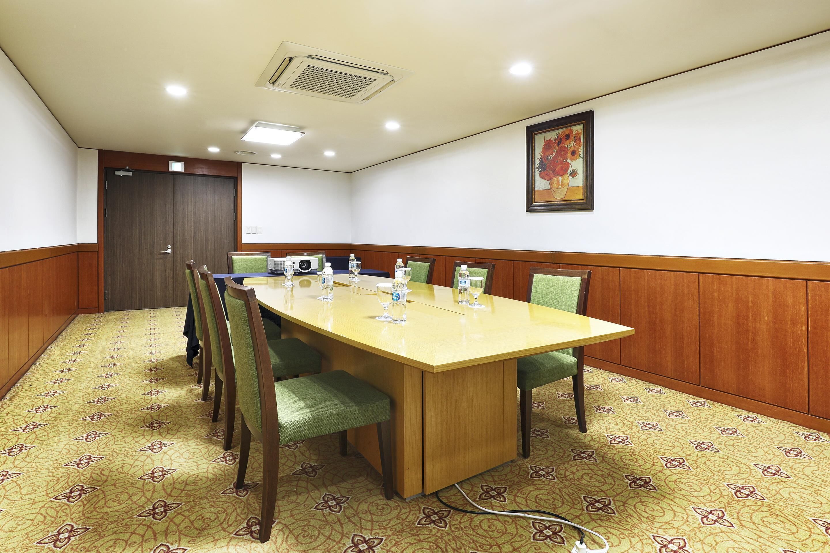 A conference room with a long table, chairs, a projector screen, and a painting on the wall.