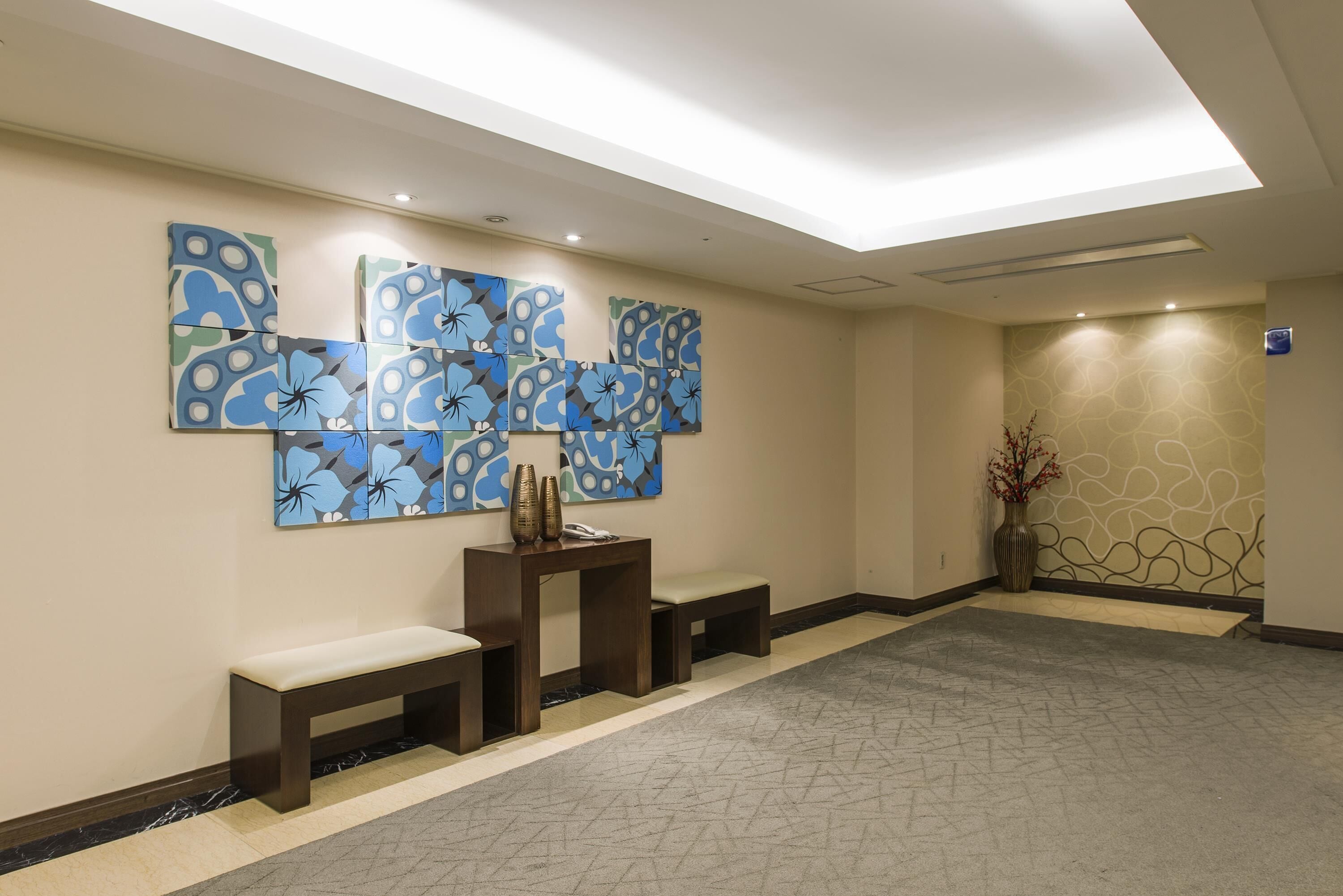 Un hall d’hôtel au design moderne, agrémenté d’une grande œuvre d’art abstraite au mur, d’un comptoir de réception et d’un espace détente avec des bancs.