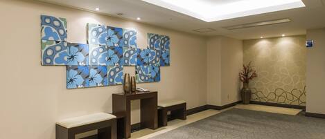 Un lobby de hotel con diseño moderno, que presenta una gran obra de arte abstracto en la pared, una recepción y una zona de estar con bancos.