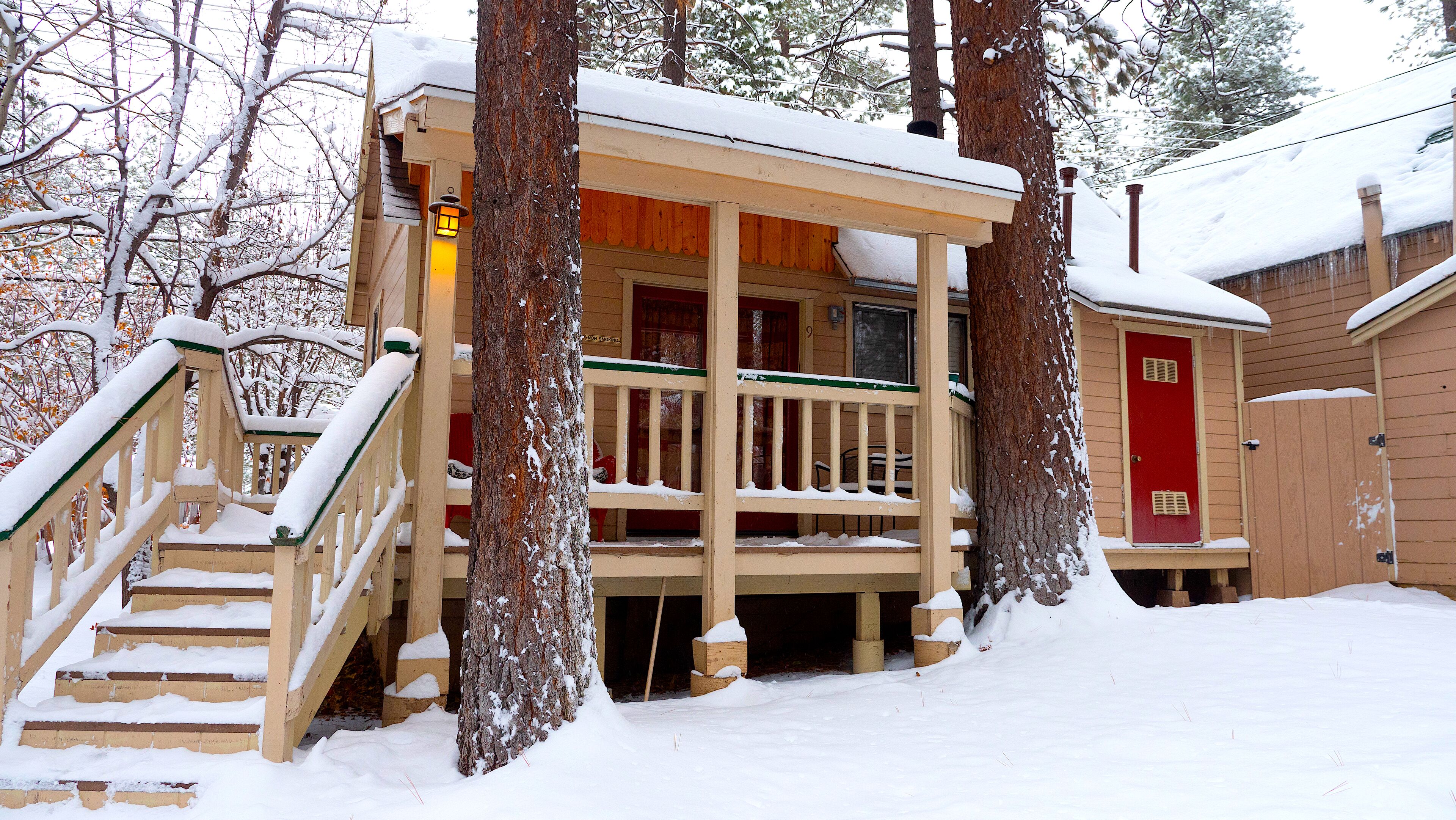 A wooden cabin with a porch, steps, and a red door.