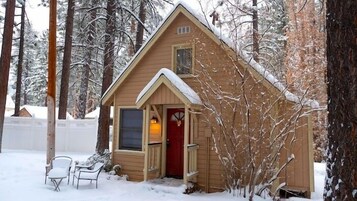 A small wooden cabin with a red door, a window, and a chair outside.