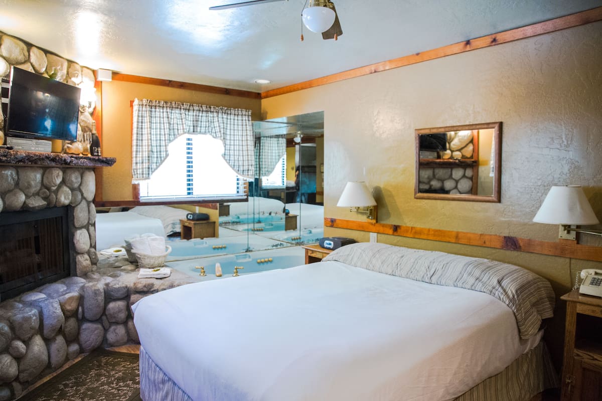 Une chambre d’hôtel avec une cheminée en pierre, un grand lit, une télévision et un miroir.