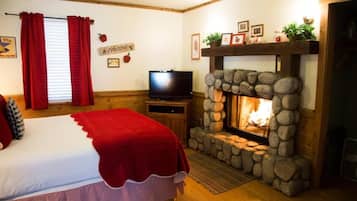 A cozy room with a bed, a television, and a stone fireplace.