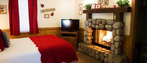 A cozy room with a bed, a television, and a stone fireplace.