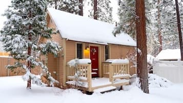 A small cabin with a red door, wooden porch, and snow-covered surroundings.