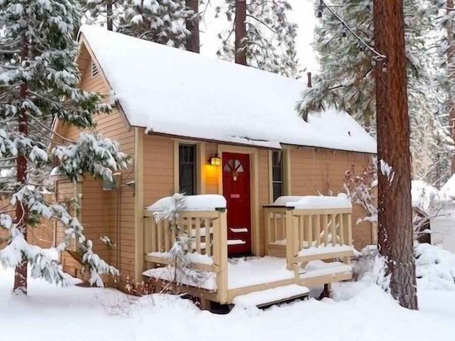A small cabin with a red door, wooden porch, and snow-covered surroundings.