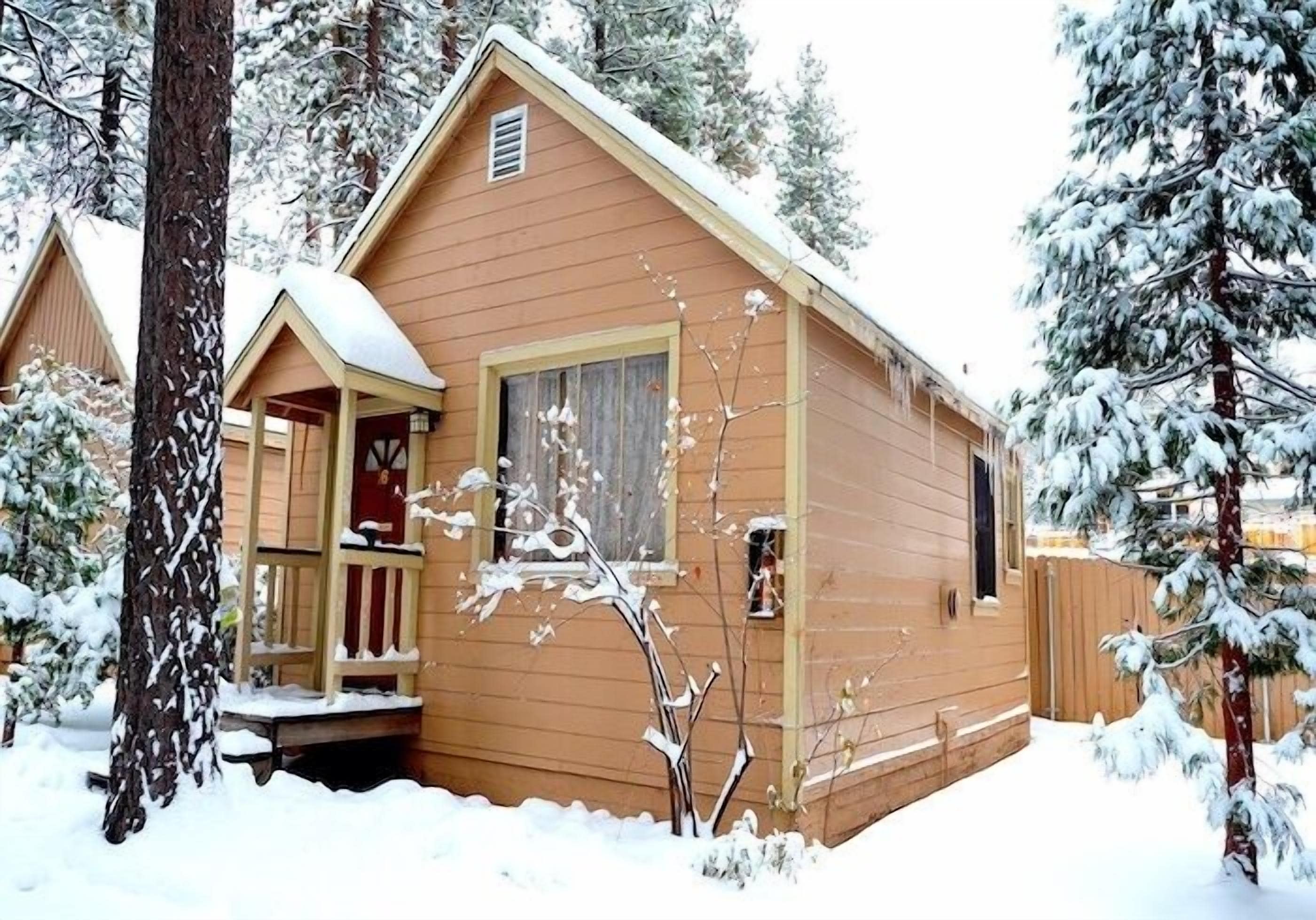 Eine Holzhütte mit Veranda, umgeben von schneebedeckten Bäumen.