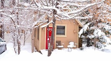 A small wooden cabin with a red door, a window, and a bench outside.