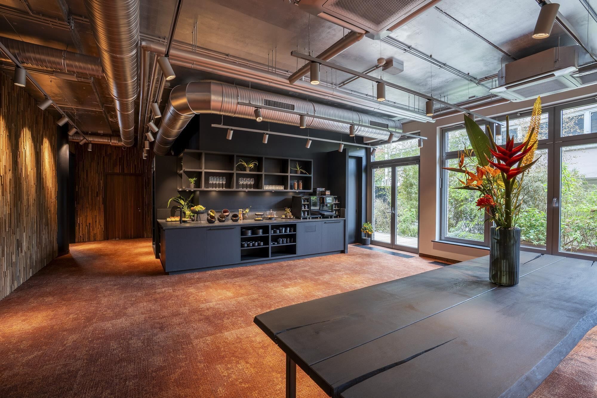 A modern kitchen with a built-in island, large windows, and a view of greenery outside.