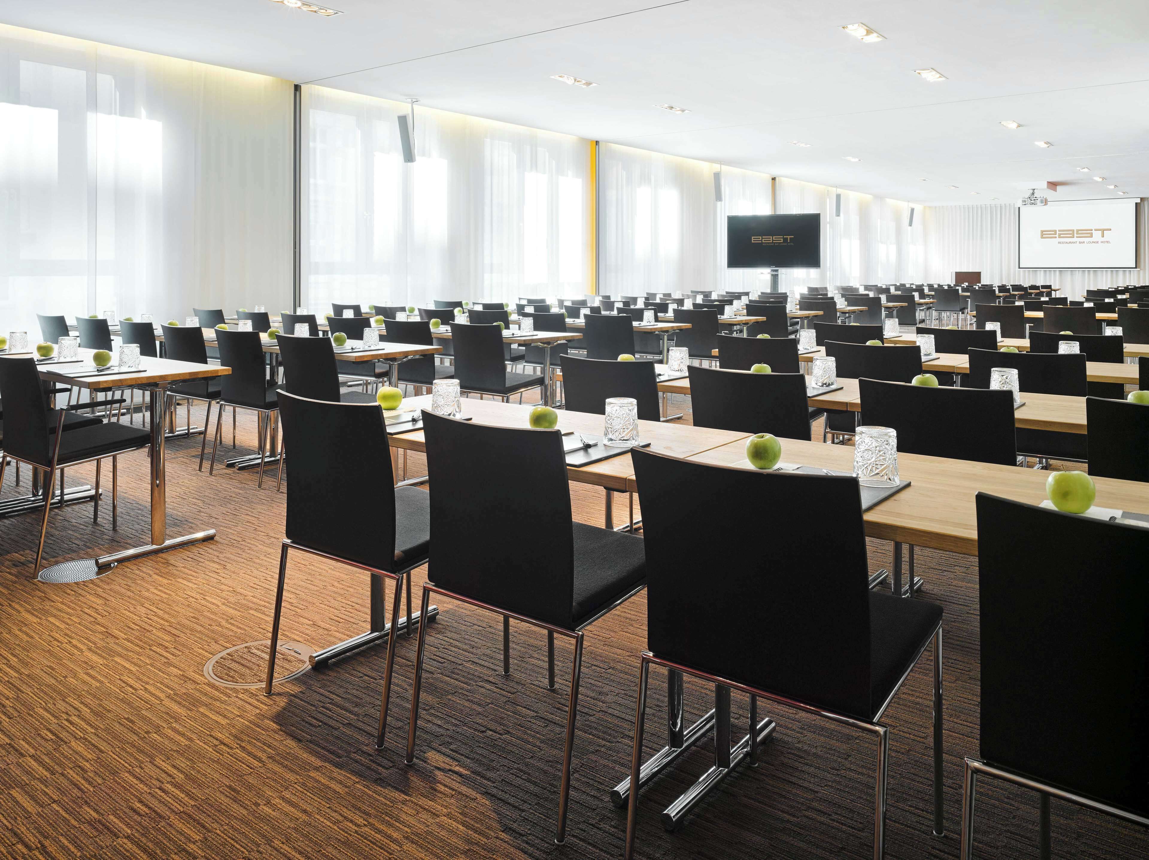 A conference room with rows of tables and chairs, a large screen, and a projection screen displaying "EAST Restaurant by LaSalle Hotel".