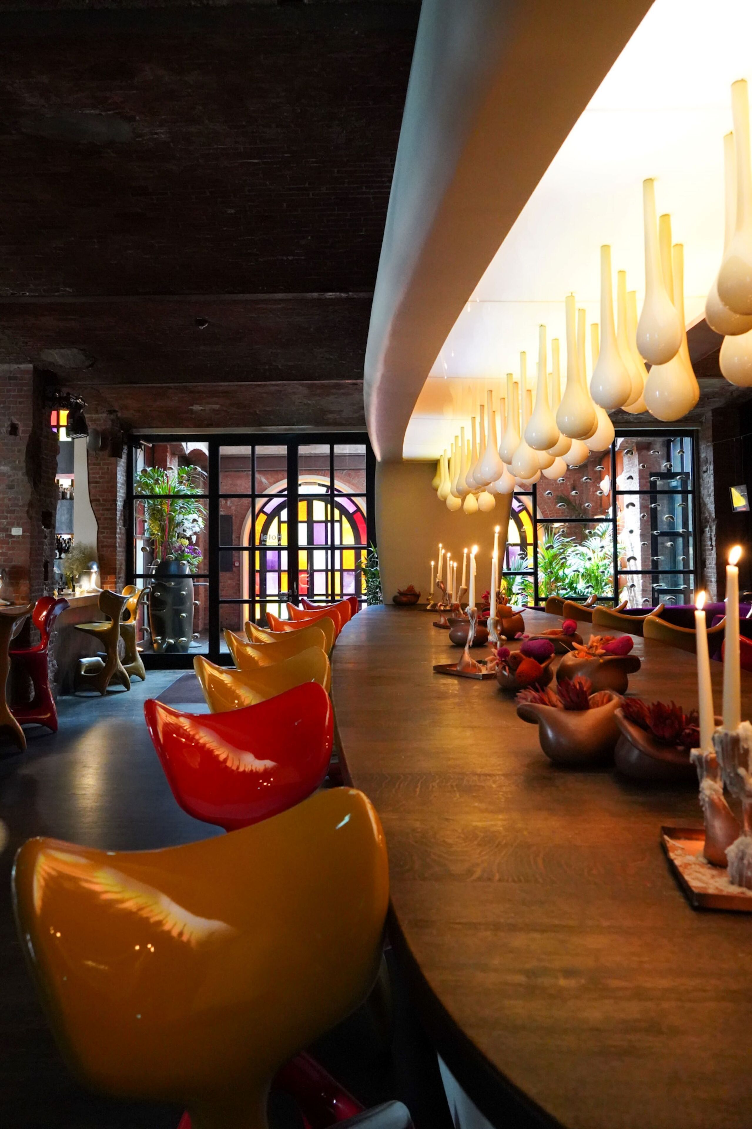 A restaurant with a long counter, unique chairs, and hanging light fixtures.