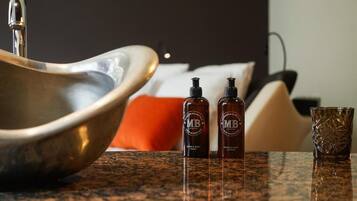 A bathroom sink, two bottles of hand and body lotion, and a glass on a granite countertop.