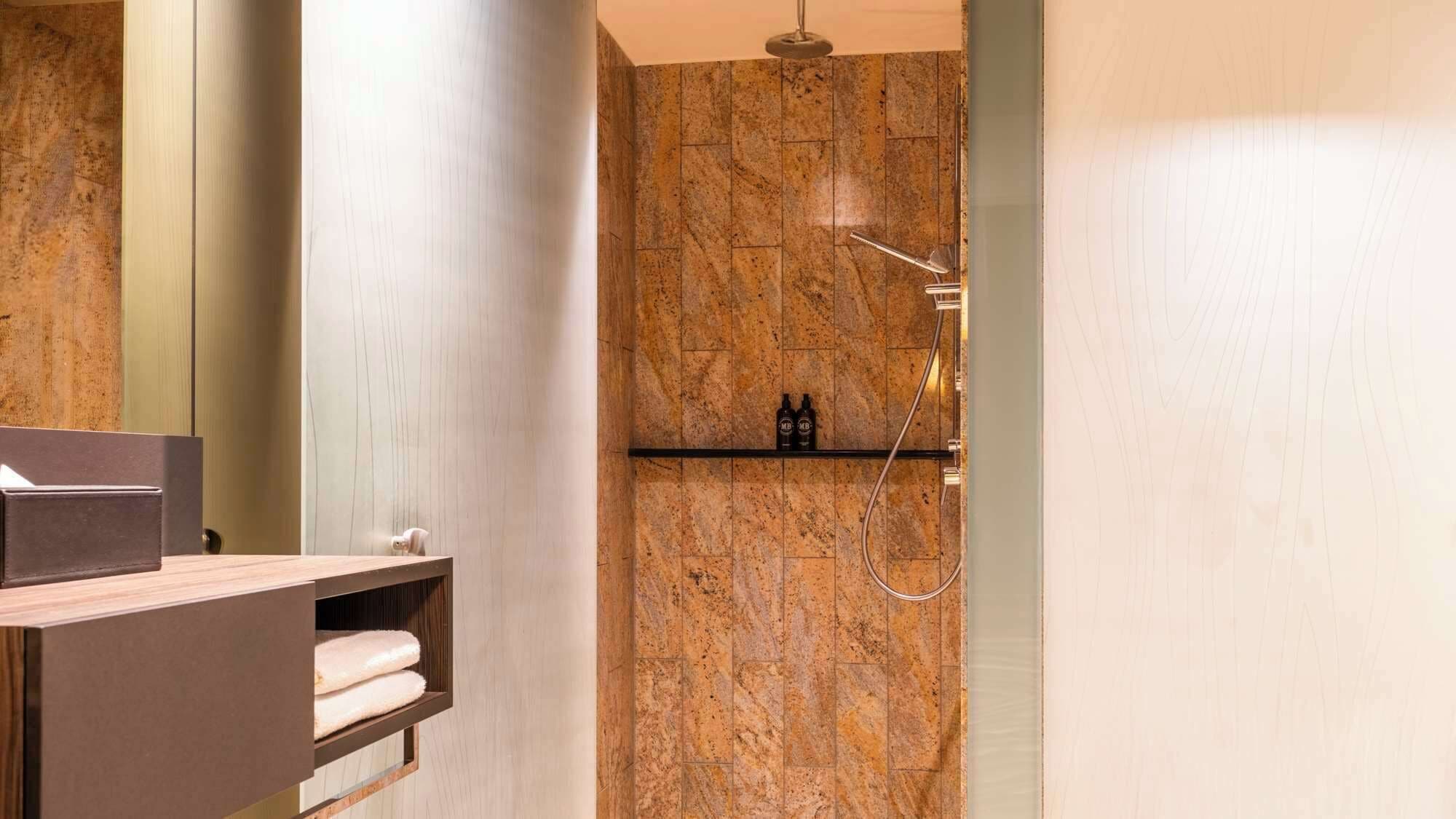 Ein modernes Badezimmer mit einer Duschwand aus Marmor, einem Handtuchhalter und einem Ablagefach für Toilettenartikel.