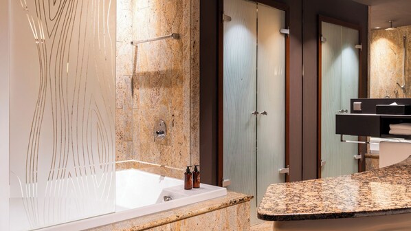 Un baño moderno con lavamanos de mármol, cabina de ducha con mampara de vidrio y tocador con espejo.