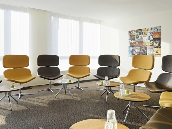 A modern waiting area with a row of chairs, tables, and a bulletin board with various posters.