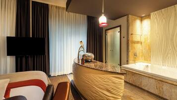 A hotel room with a bed, a TV, a bathroom with a bathtub, and a counter with a sink.
