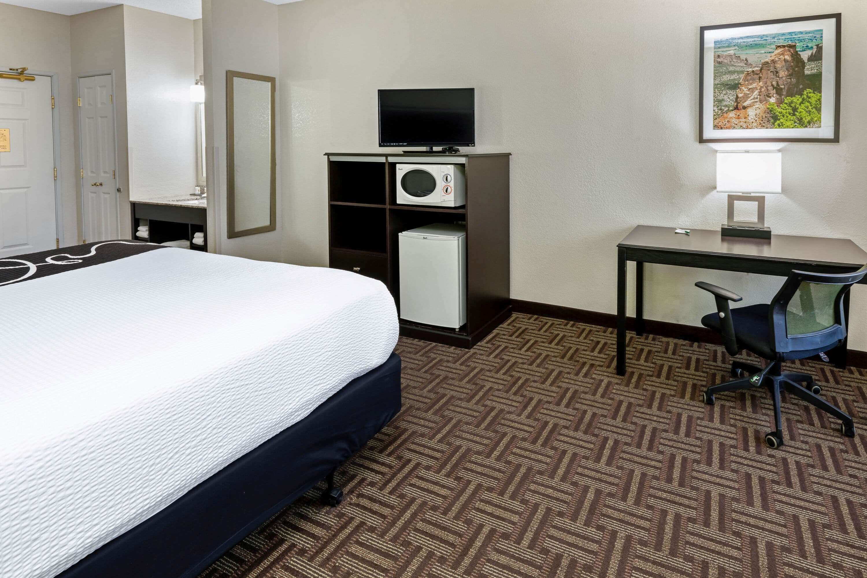 A hotel room with a bed, a desk, a chair, a television, a refrigerator, and a picture on the wall.