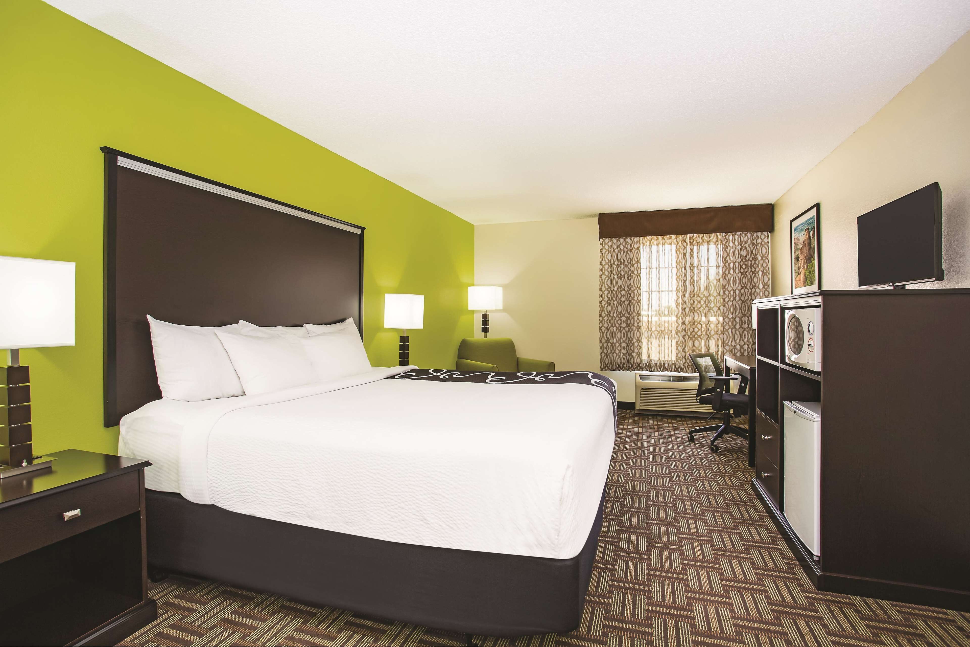A hotel room with a large bed, two bedside lamps, a desk with a chair, a television, and a minibar.