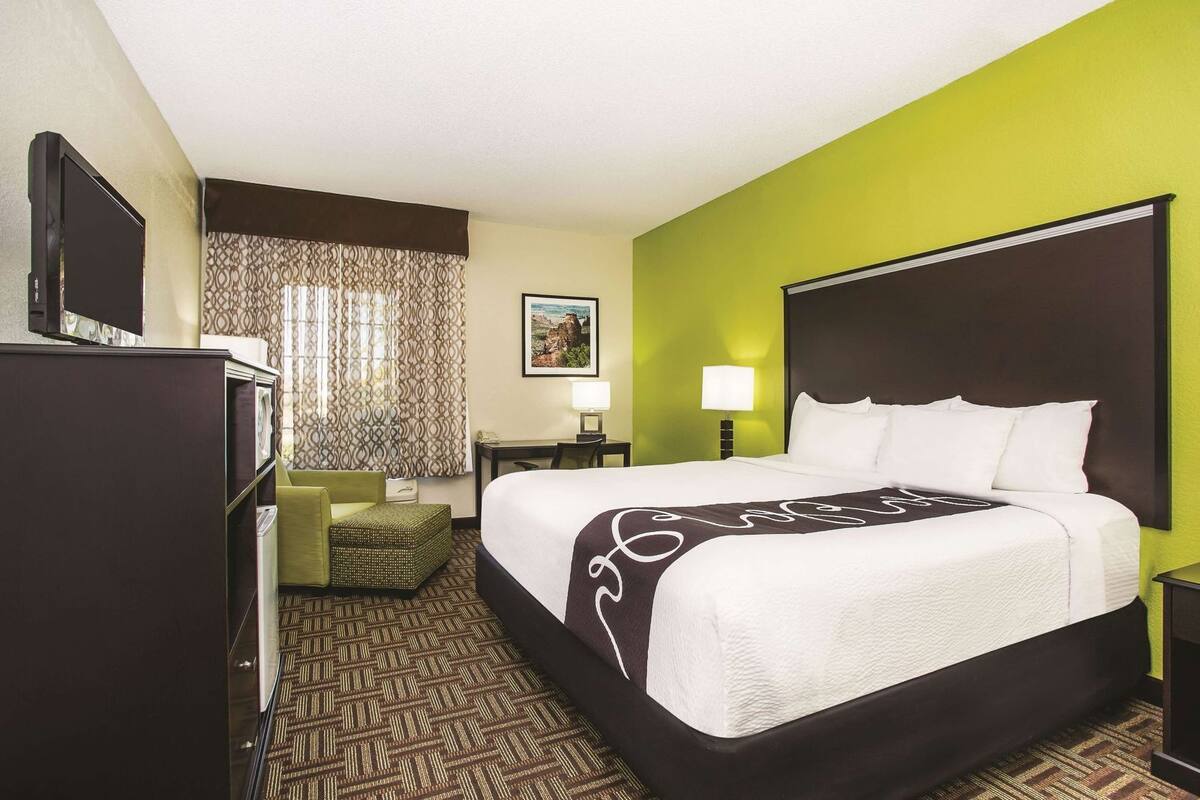 Ein Hotelzimmer mit Bett, Schreibtisch, Stuhl, Fernseher und einem fensterbepflegten Fenster.