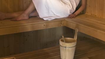 Eine Person in einer Sauna mit Holzbänken und einem Holzwascheimer.