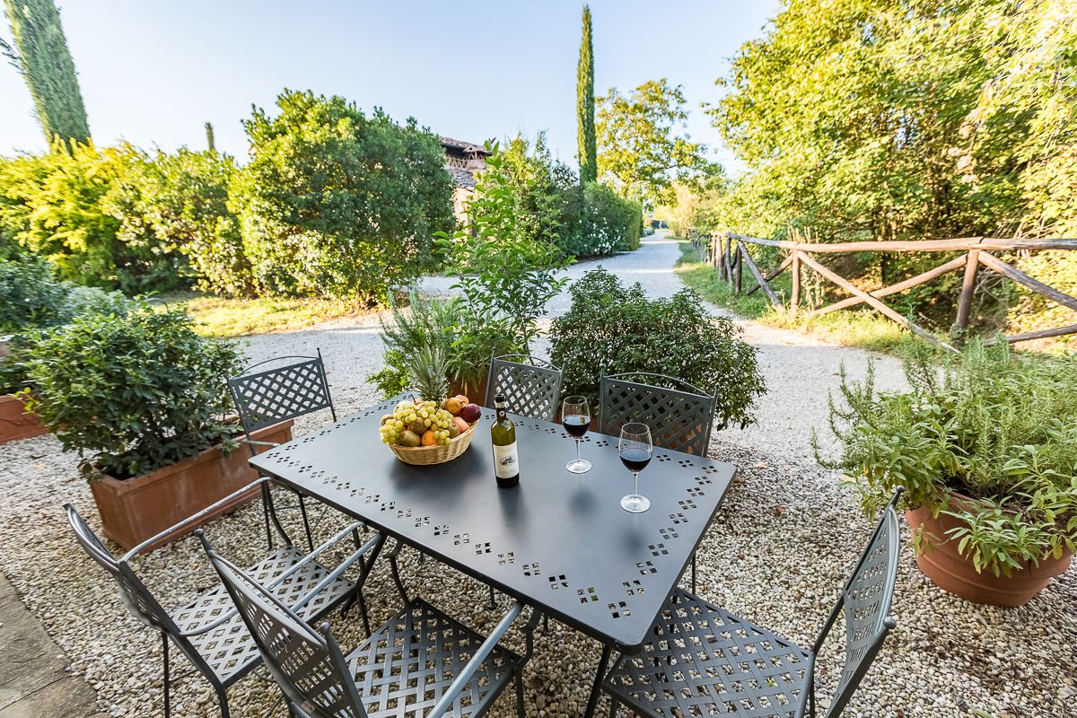 An outdoor patio with a table set for two, surrounded by potted plants and a gravel path.