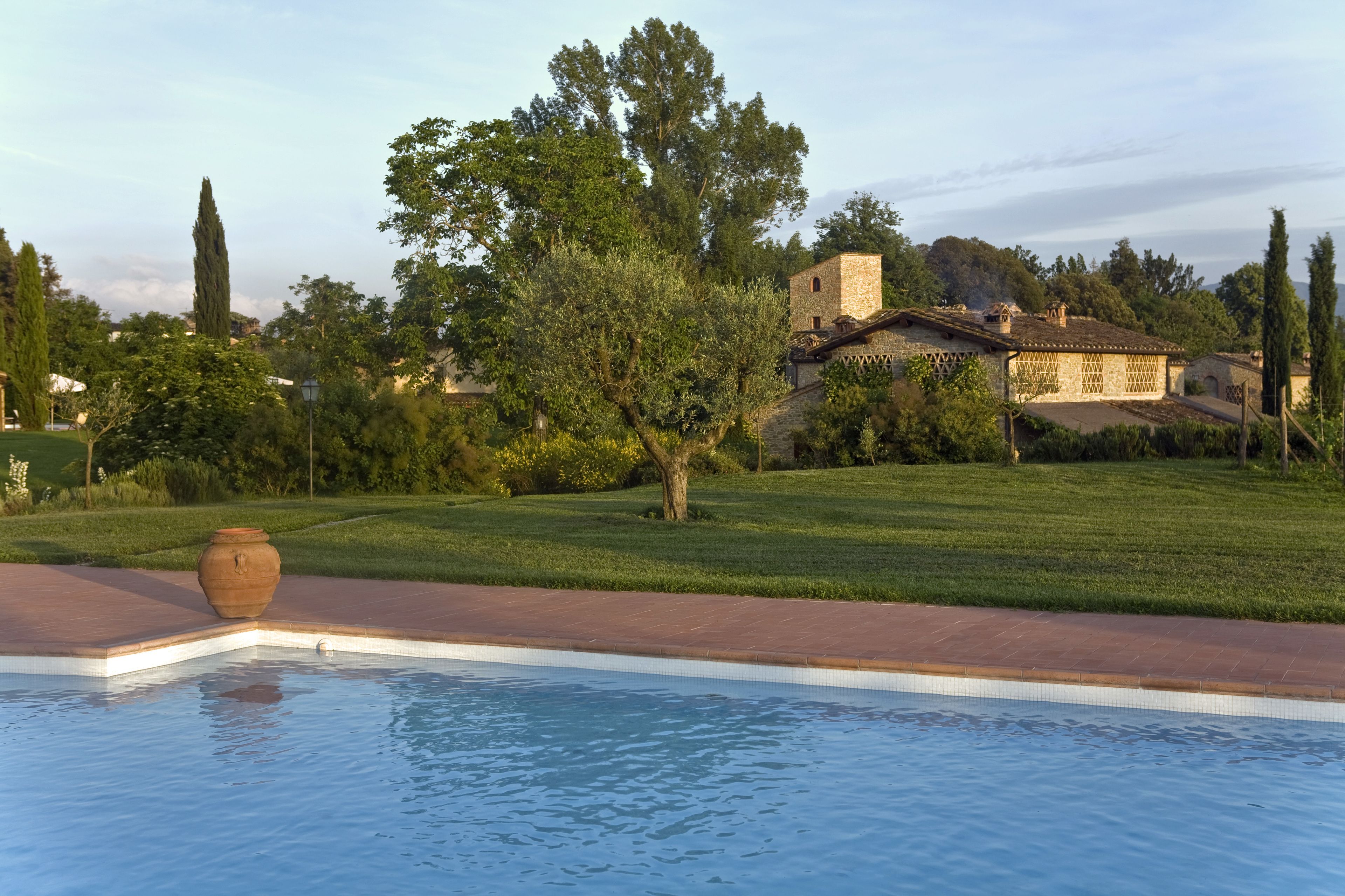 A swimming pool with a stone vase, surrounded by a well-maintained lawn and a stone building in the background.