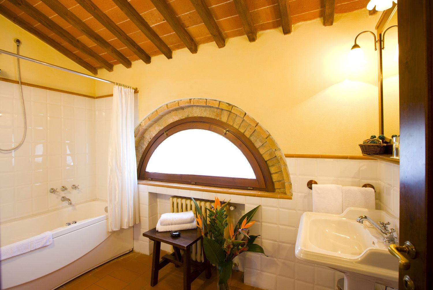 A bathroom with a bathtub, a sink, and a shower. There is a window with an arch above the sink and a towel rack above the bathtub.