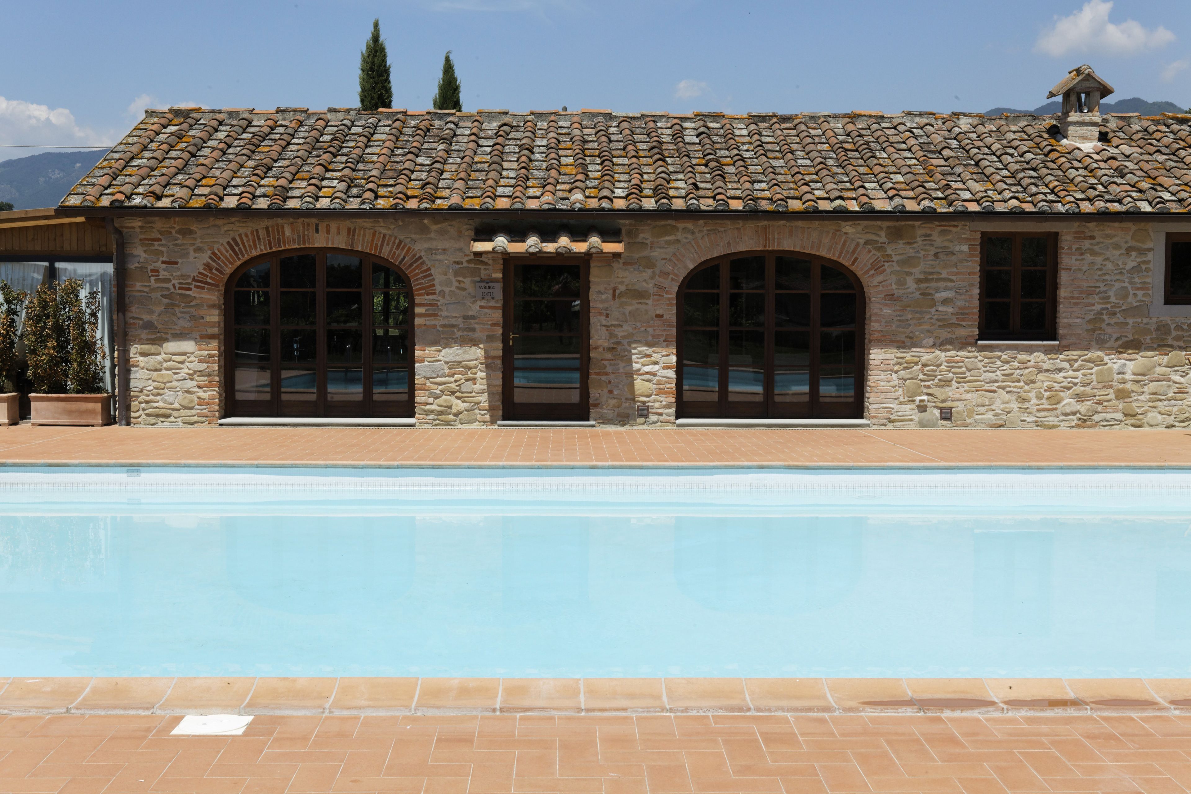 A stone building with a tiled roof and a swimming pool in front.
