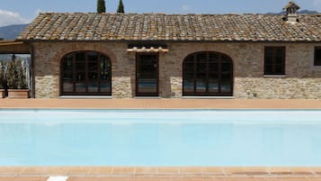 A stone building with a tiled roof and a swimming pool in front.