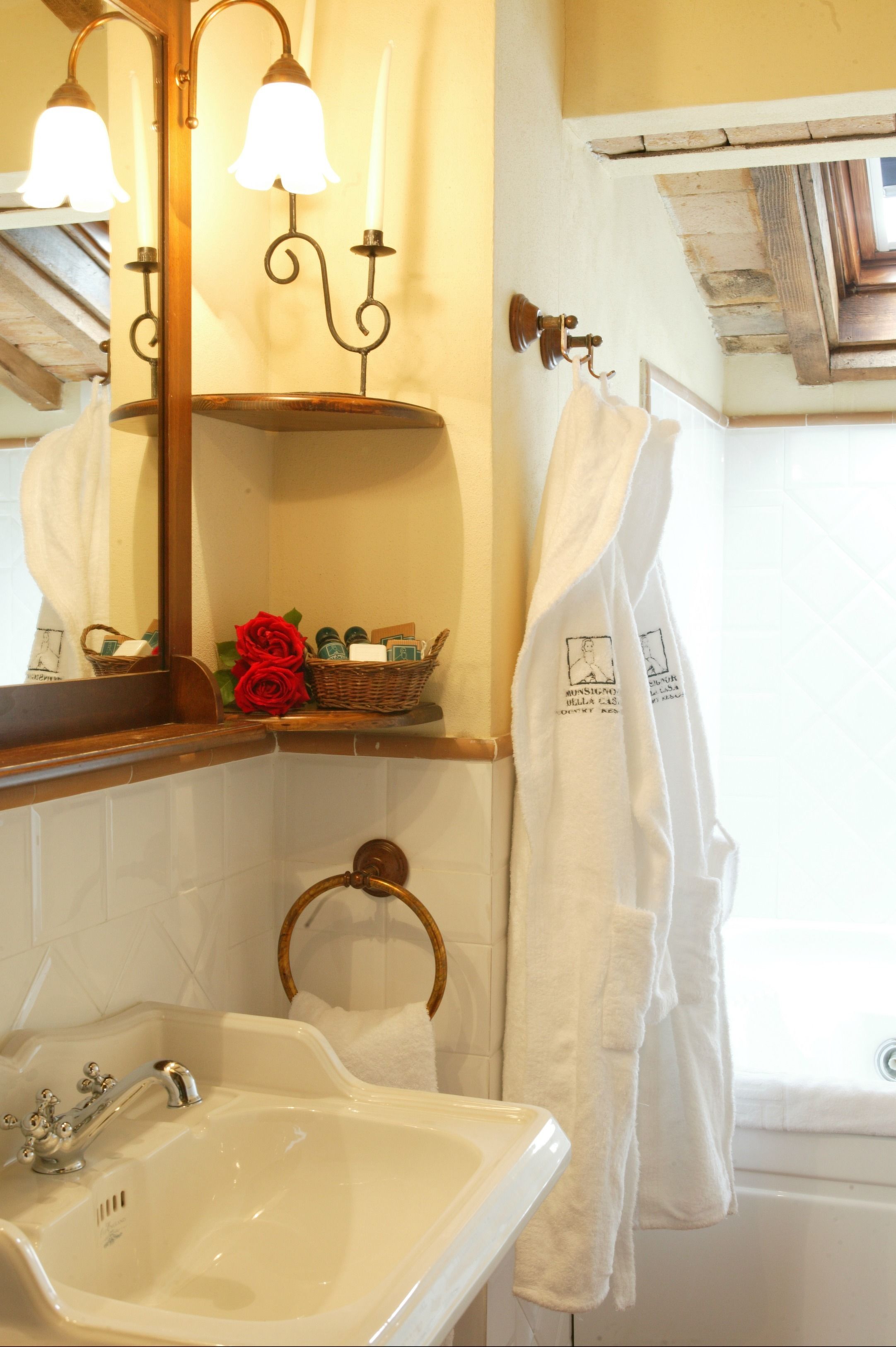 Une salle de bain avec un lavabo, un miroir, un porte-serviettes et une étagère sur laquelle se trouvent un panier et des roses.