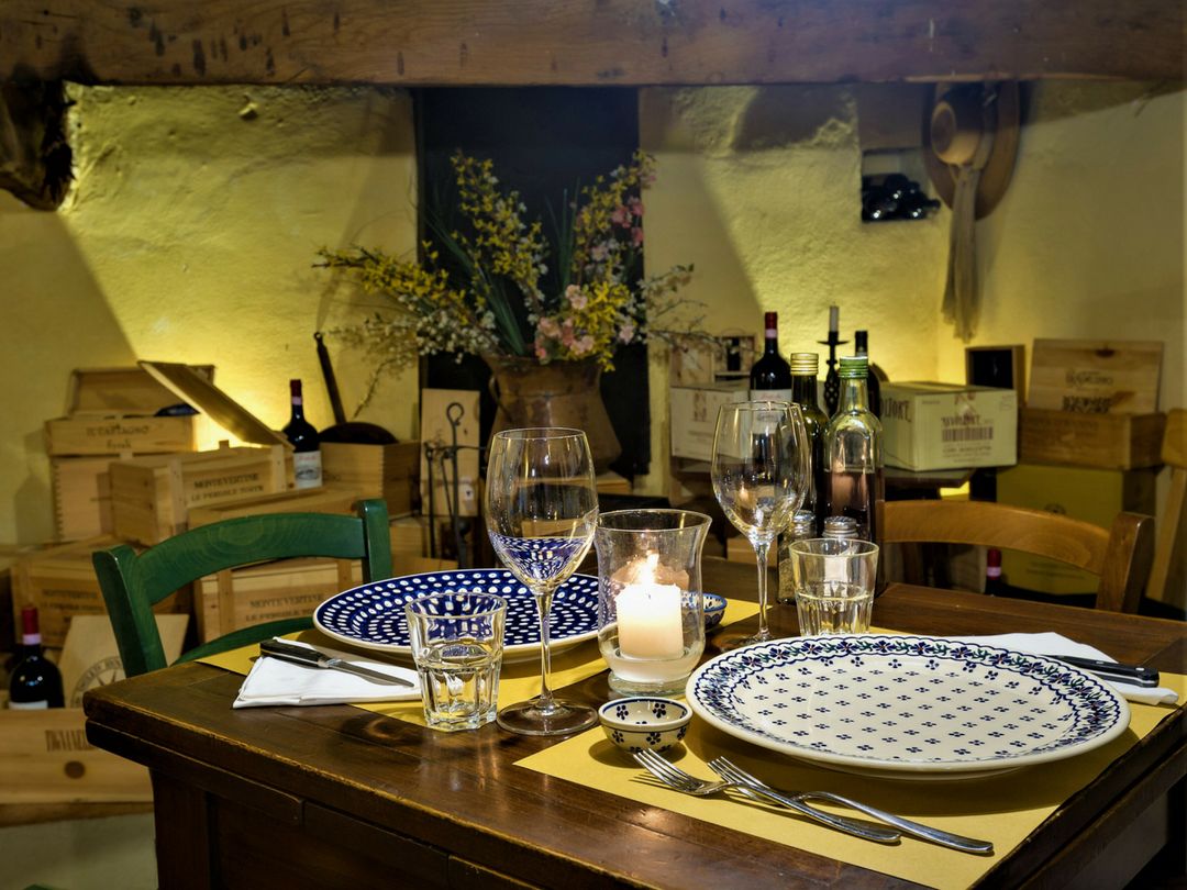 Une table à manger dressée avec des assiettes, des verres et une bougie, entourée de caisses en bois et d’un vase rempli de fleurs.