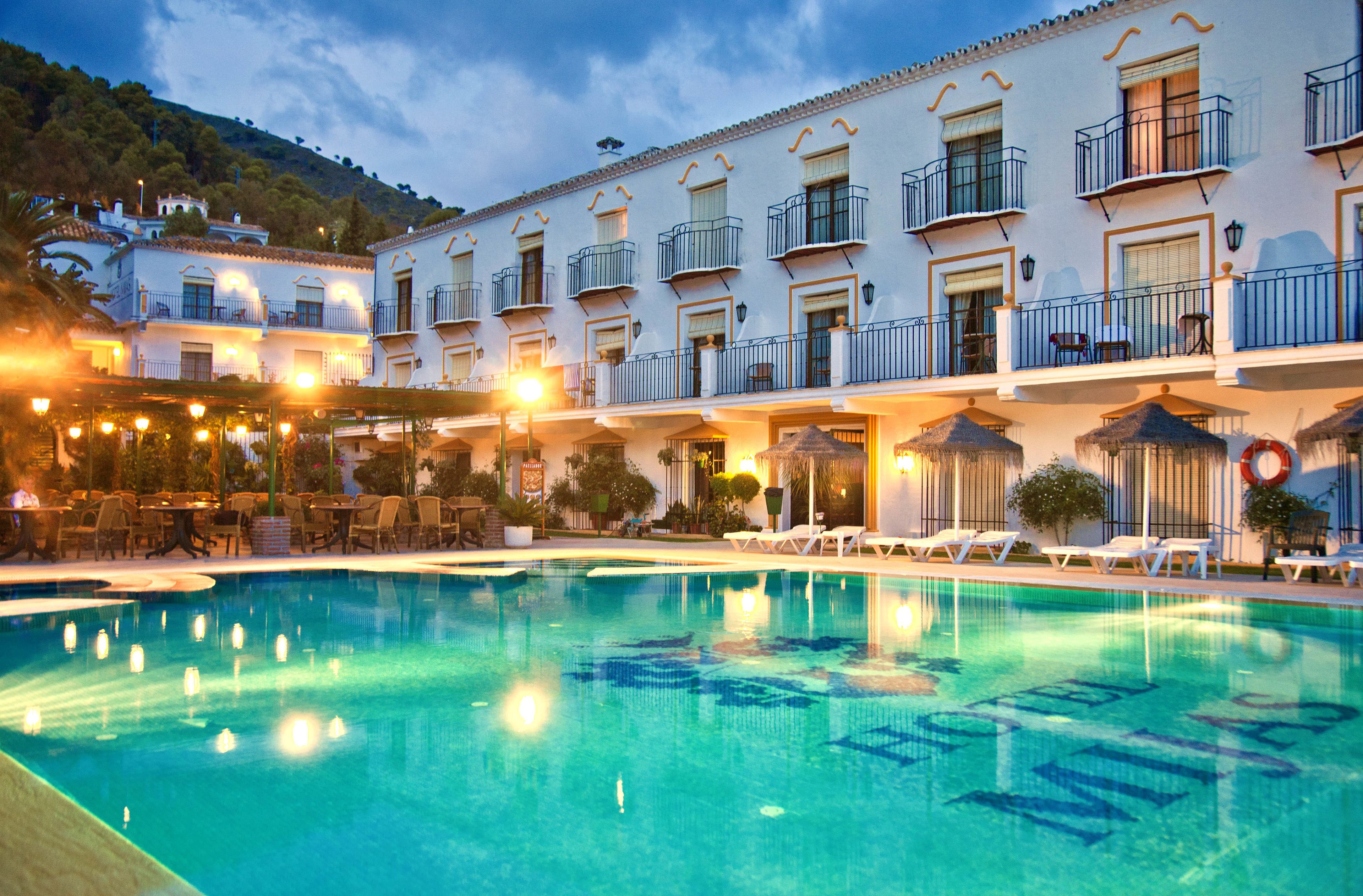 A hotel with a swimming pool, outdoor seating, and a hillside view.