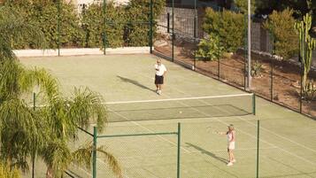 Una cancha de tenis con red, rodeada por una valla y árboles.