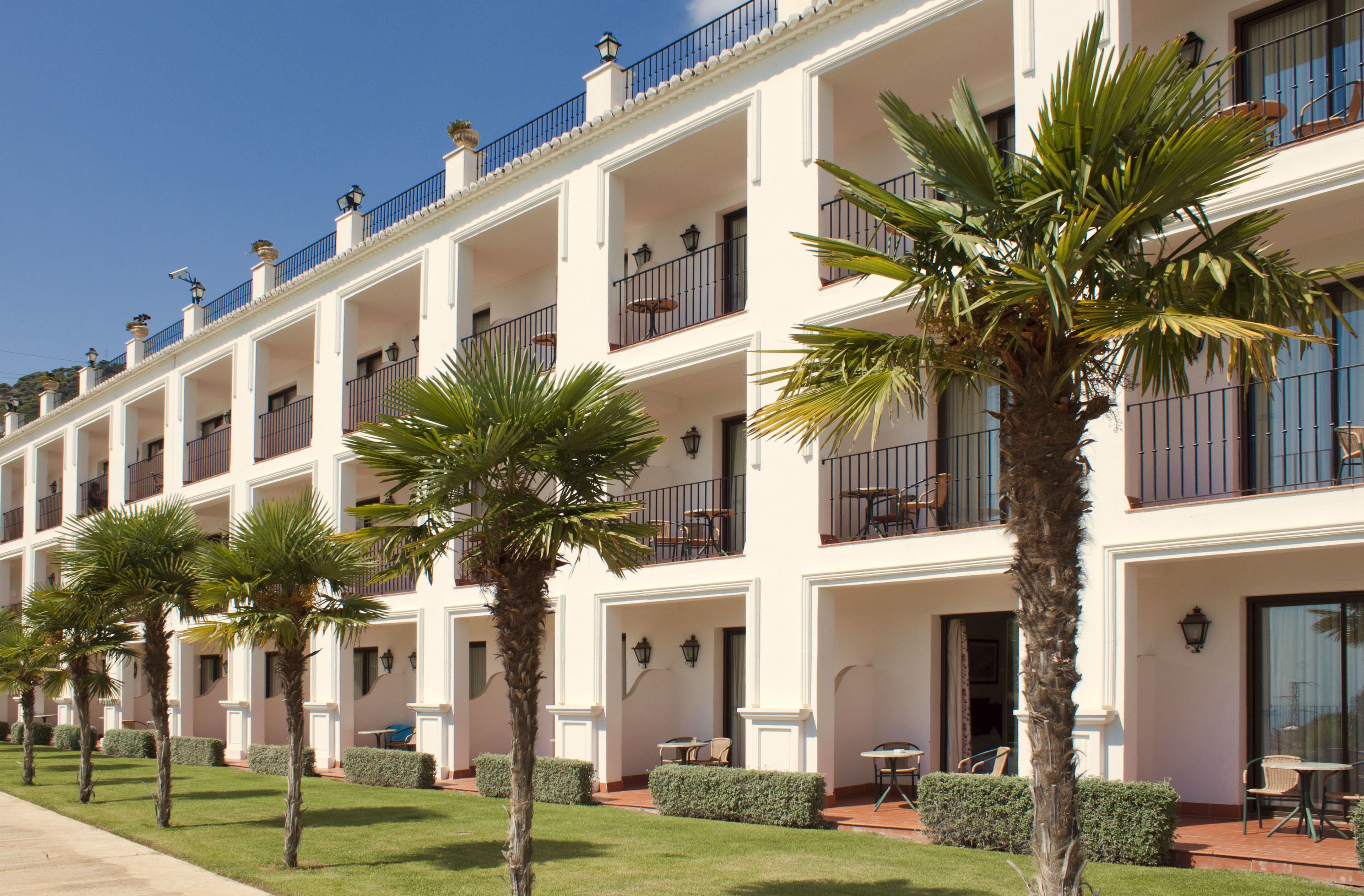 A multi-story hotel with balconies, outdoor seating, and palm trees.
