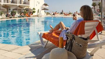 A poolside area with lounge chairs, a pool, and a building with balconies.