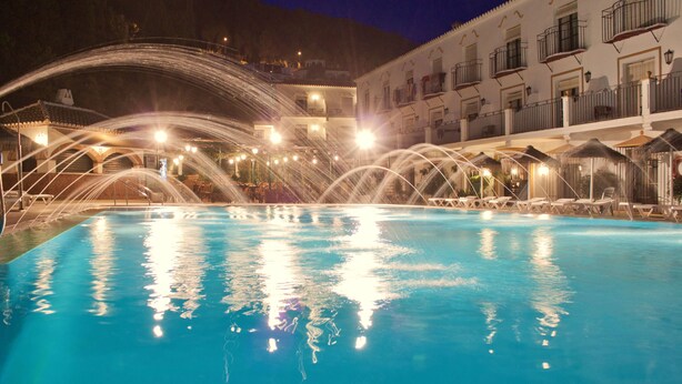 Una piscina con fuentes, sillones de descanso y un edificio con balcones al fondo.