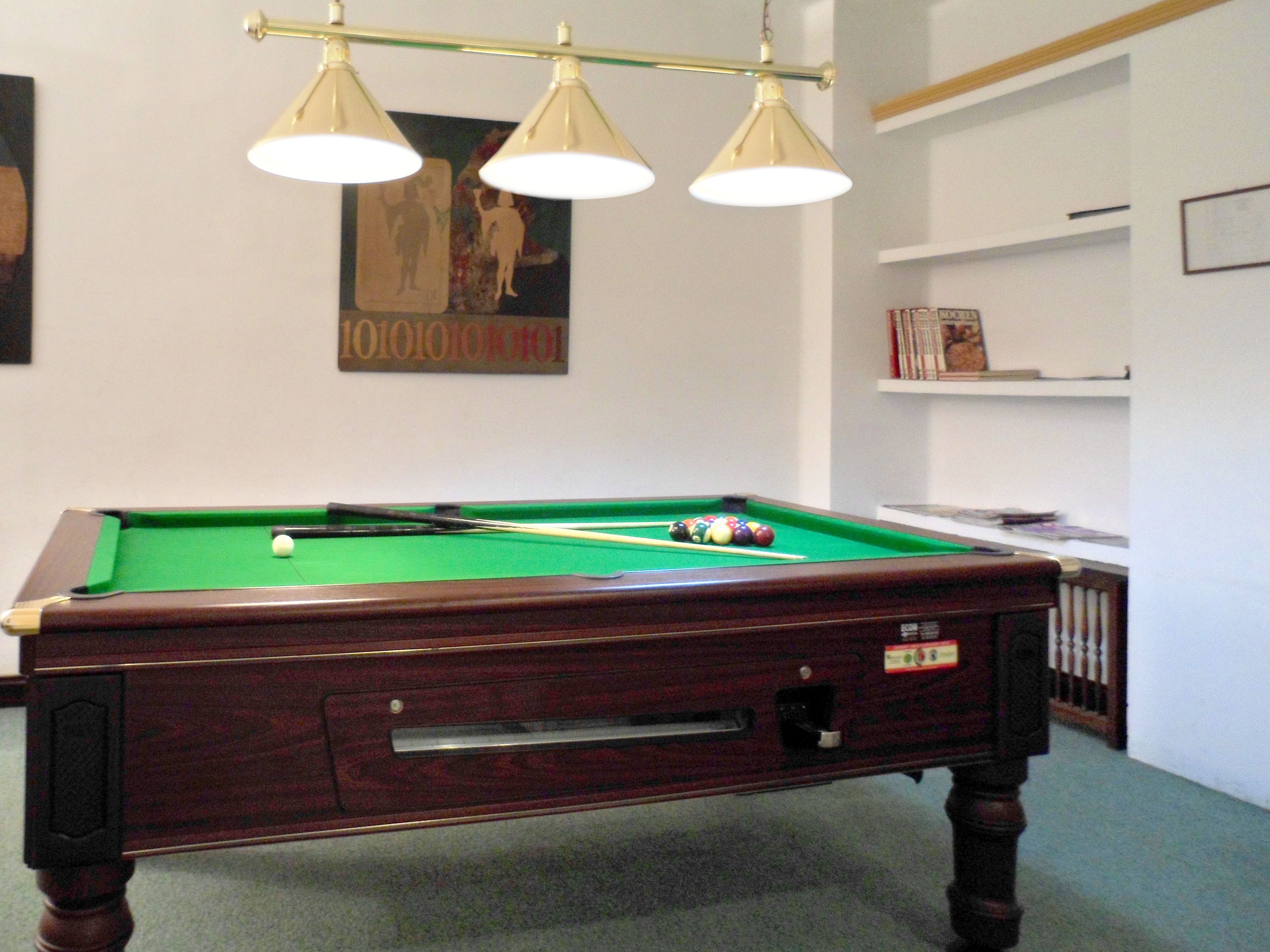 A pool table with three overhead lights, a framed poster, and a bookshelf in a room.