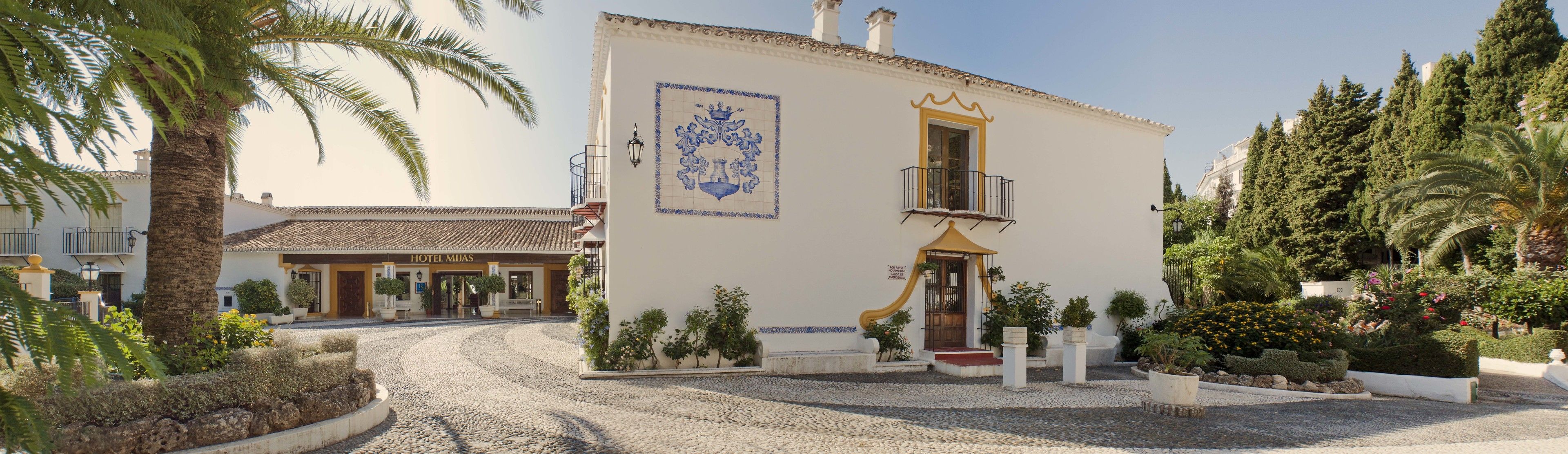 Un bâtiment traditionnel doté d’un porche carrelé, d’un balcon et d’une cour intérieure agrémentée de plantes et d’un palmier.