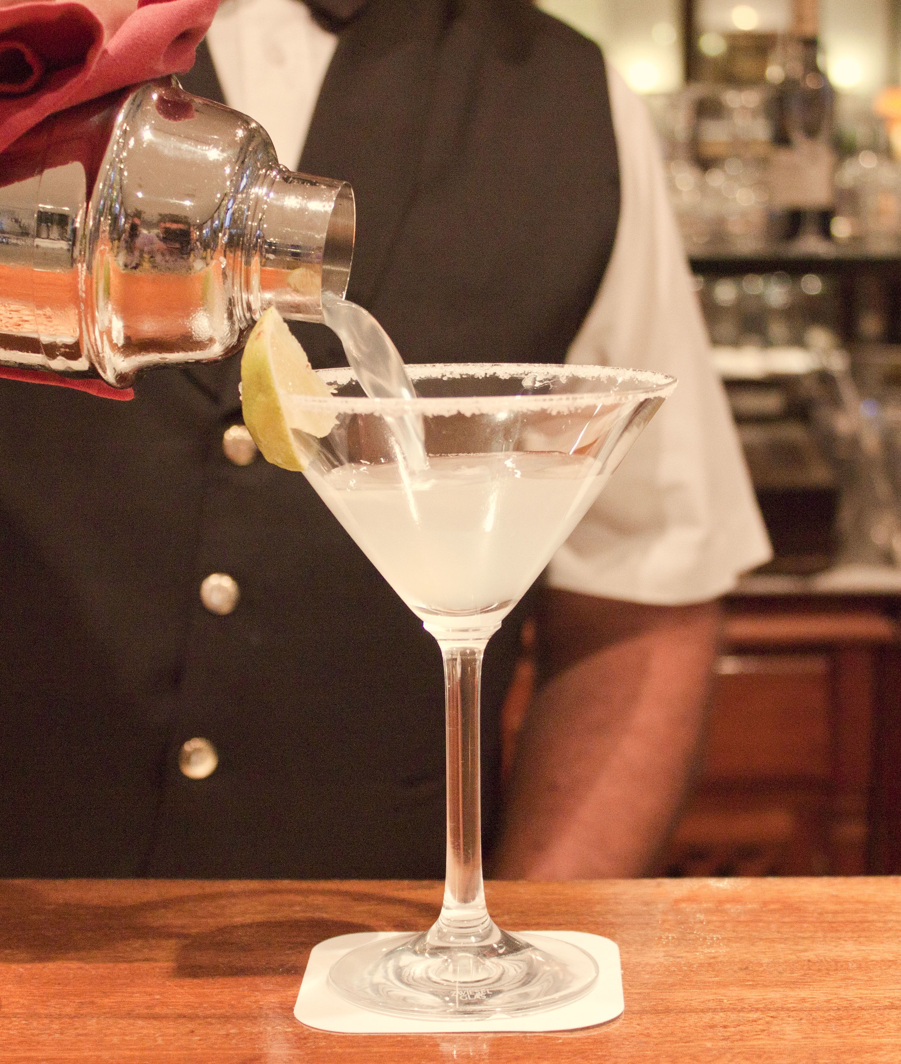 A bartender pouring a drink into a martini glass with a lime wedge.