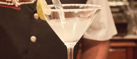 A bartender pouring a drink into a martini glass with a lime wedge.