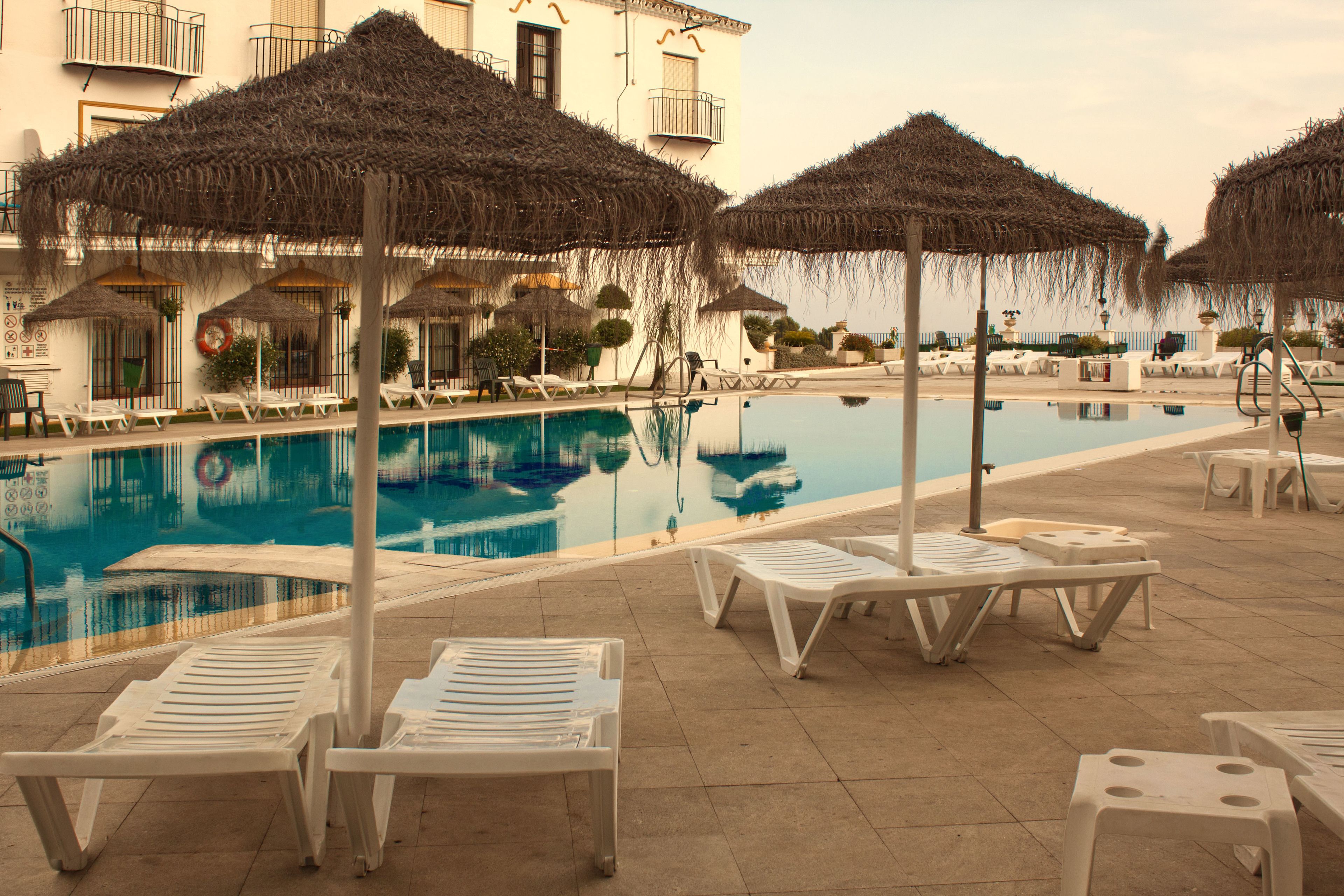 A pool area with lounge chairs and thatched umbrellas, surrounded by a building with balconies.