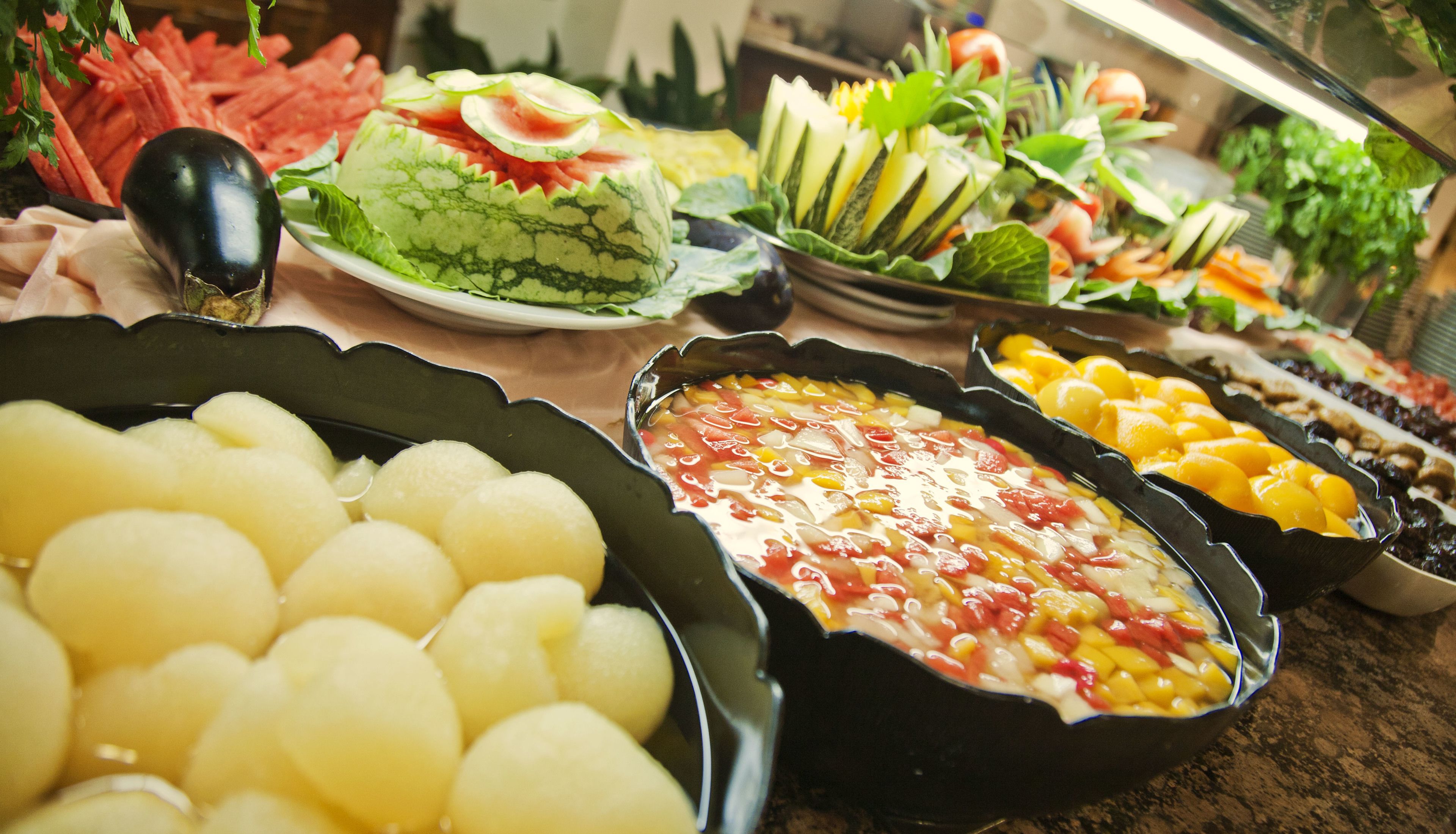 A buffet with various dishes including fruits, vegetables, and a salad.