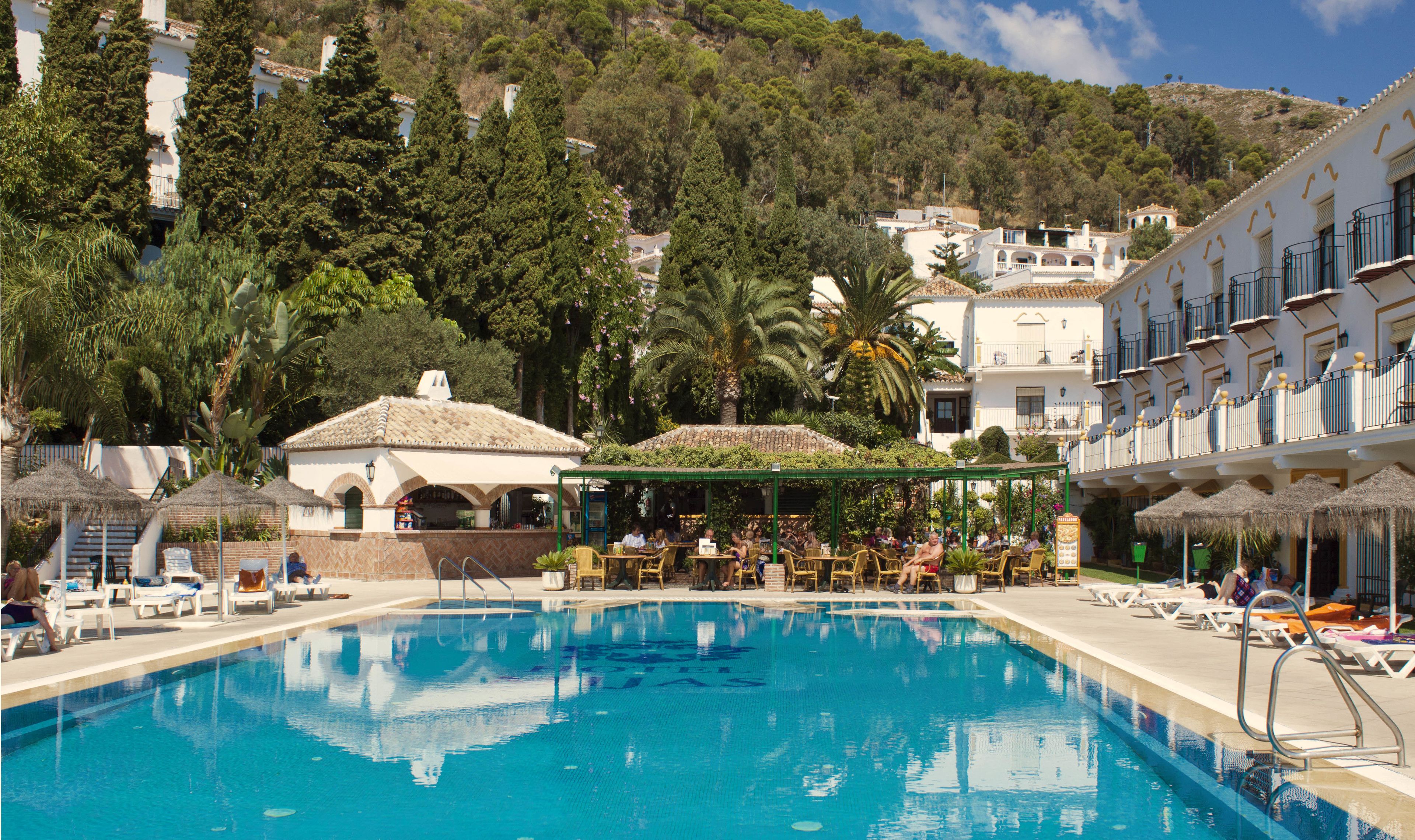 A swimming pool with lounge chairs and umbrellas, surrounded by buildings and trees.