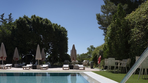 A swimming pool with lounge chairs and umbrellas, surrounded by trees. - Sercotel Riscal (Puerto Lumbreras)