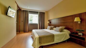 Una habitación de hotel moderna con una cama grande, un televisor montado en la pared y una mesita de noche con una lámpara y un teléfono.