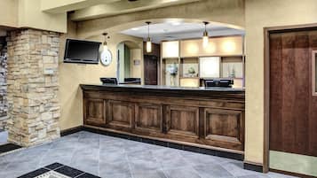A reception area with a stone wall, a wooden reception desk, a flat-screen TV, a clock, and a decorative vase.